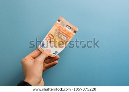 hand holding a 50 euro bill on a blue colored background. Money, finance, wealth, business concept.