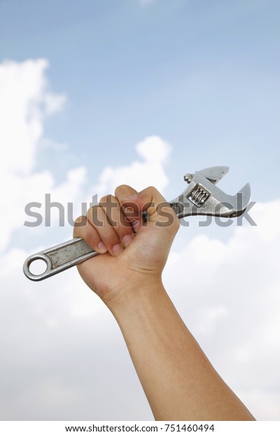 Hand holding adjustable spanner wrench with\
sky background