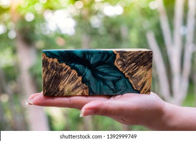 Hand holding Afzelia burl wood bar casting with epoxy resin Stabilizing for blanks on bokeh abstract background