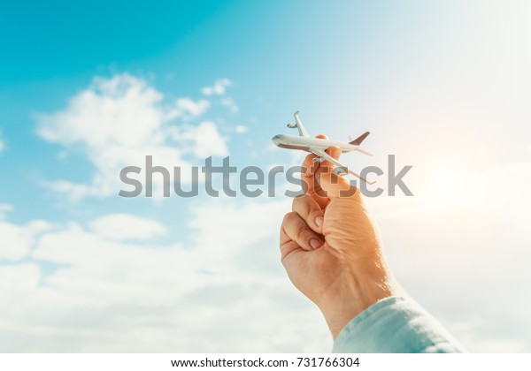 hand holding airplane model in\
front of cloudy blue sky background. air transportation\
concept.