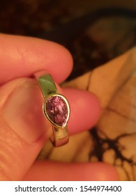 Hand holding an Alexandrite set in a ring under incandescent light showing the red colour change