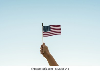 Hand holding American flag in air against sky - Powered by Shutterstock