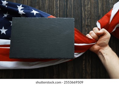 Hand Holding American Flag with Blank Slate for Patriotic Messages, Wooden Background - Powered by Shutterstock