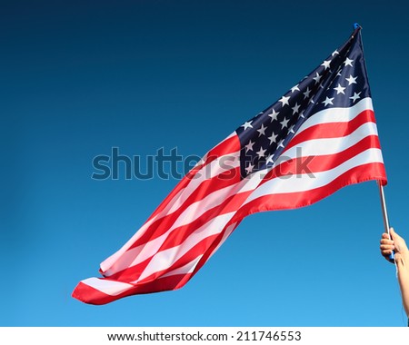 Hand holding american flag on the blue sky background