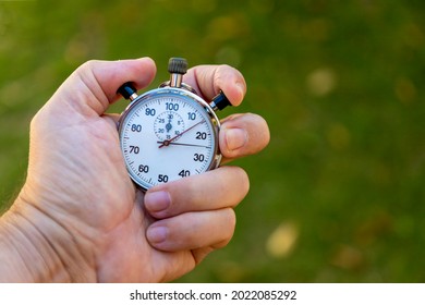 Hand Holding Antique Stopwatch With Blurred Green Background.