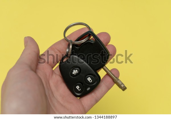 Hand holding auto key and remote above the\
yellow background. Success in\
business