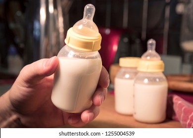Hand holding baby bottle filled with milk or formula.