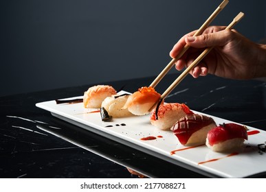 Hand holding bamboo chopsticks a elegant piece of sushi while soaking it in soy sauce at restaurant. Front view. Japanese cuisine concept.