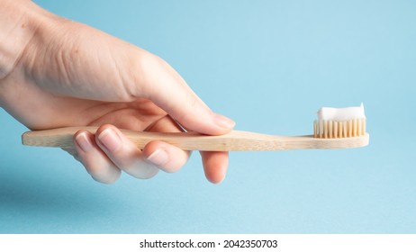 Hand holding bamboo toothbrush on blue. Holding wooden eco toothbrush. Natural toothpaste on a bamboo toothbrush - Powered by Shutterstock