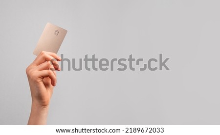 Hand holding bank card with chip over gray ad background with copy space for text.