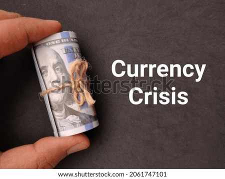 Hand holding banknotes with text Currency Crisis on a black background.