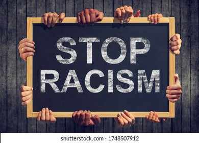 A lot of hand are holding a banner with text " Stop racism" on dark background. Different people express one common opinion Stop Racism