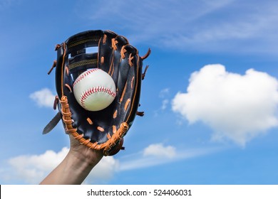 Hand holding baseball in glove with blue sky