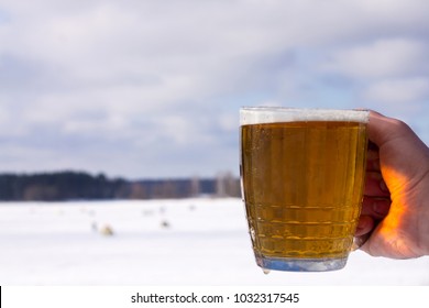 Hand Holding Beer In A Glass Cup, Winter, Sunny Day, Ice Fishing At The Background