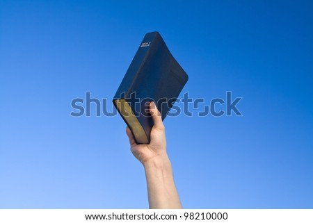 Hand holding Bible over blue sky