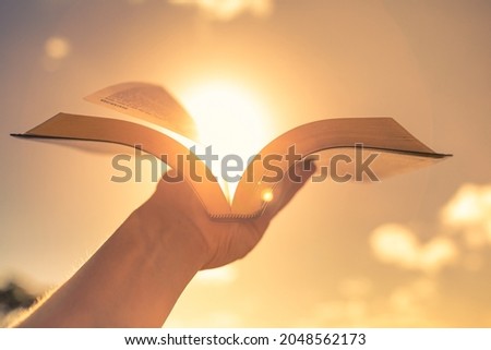 Hand holding bible up to the sun light. 