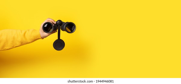 hand holding binoculars over yellow background, panoramic image - Shutterstock ID 1944946081