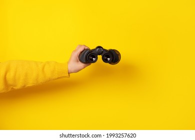 hand holding binoculars over yellow background - Shutterstock ID 1993257620