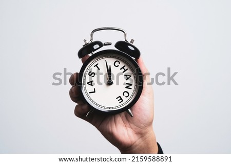 Hand holding black alarm clock which inside last chance wording for time and opportunity concept.