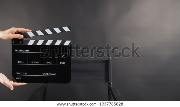 A\
hand is holding black clapper board or movie slate and director\
chair on black background. It has written in\
number.