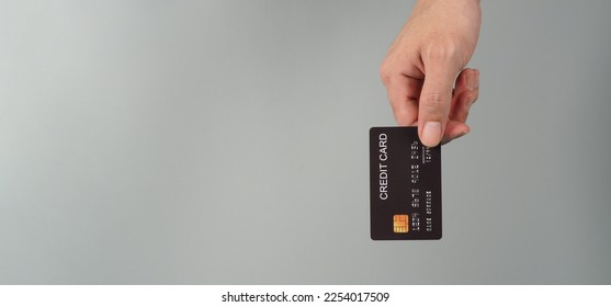 Mano sostiene una tarjeta de crédito negra aislada en un fondo gris.