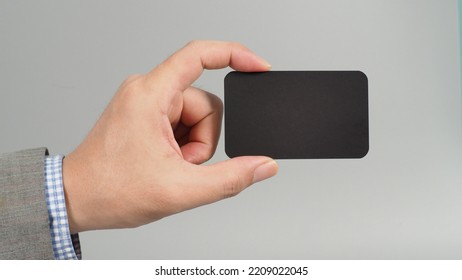 Hand Is Holding Black Empty Card And Wear Suit On Gray Background. Business Man Concept. Copy Space For Text