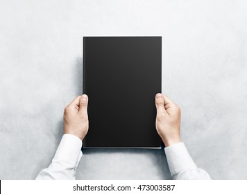 Hand holding black magazine with blank cover mockup. Arm in shirt hold journal clear template mock up. A4 book softcover surface design. Paperback print display show. Closed notebook cover showing.