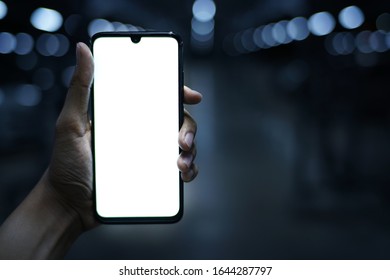 Hand Holding Black Phone At Night Blur Background And Copy Space    