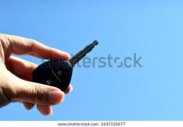 hand holding black remote car key with blue\
sky background.