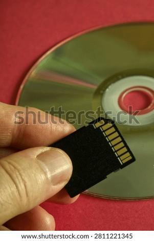 Hand holding a black sd memory card over a reflective dvd surface on red background