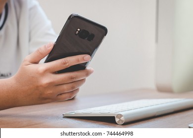 Hand Holding Black Smart Phone On Back View In Workspace