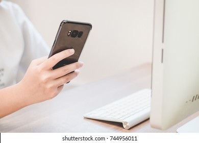 Hand Holding Black Smart Phone On Back View In Workspace