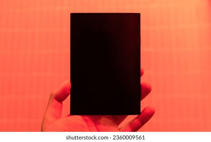 Hand holding a blank cover of book with red neon light. Mock Up Template. - Powered by Shutterstock