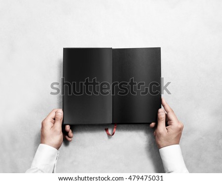 Hand holding blank opened book mock up with black pages. Person reading empty paperback mockup. Black notebook inside template. Publication design leafing man. Textbook spread with bookmark.