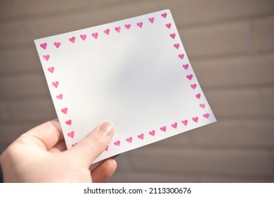 Hand Holding Blank Paper with a Border of Pink Hearts