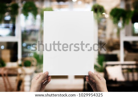Hand holding blank paper poster design for menu at restaurant, Mock up space for display of menu or design.
