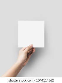 Hand Holding Blank Paper Sheet Square Size On Grey Background.