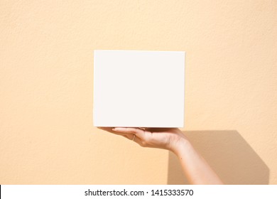 Hand holding blank white box mockup give gift on yellow and orange background, copy space, text, beauty woman hand.