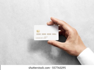 Hand Holding Blank White Credit Card Mockup With Chip And Embossed Gold Info. Plain Plastic Bank-card Display Front, Design Mock Up. Electronic Money Holder Template.