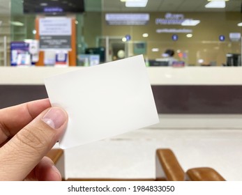 Hand holding blank white cue card with blurred cashier counter background, Young man showing blank ticket card and waiting for the queue