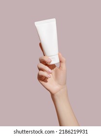 Hand holding blank white plastic tube on pink background. Cosmetic beauty product branding mockup. Copy space. High quality photo