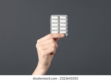 Hand holding blister pills on dark gray background - Powered by Shutterstock