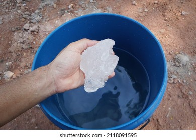 Hand Holding A Block Of Alum To Stir The Cloudy Water In The Bucket To Make It Clear.