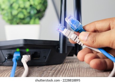 Hand holding Blue and white  Cable Network  RJ45 Lan Internet. router and laptop placed on a wooden table, modem router, Data Center Concept. - Shutterstock ID 2228818895