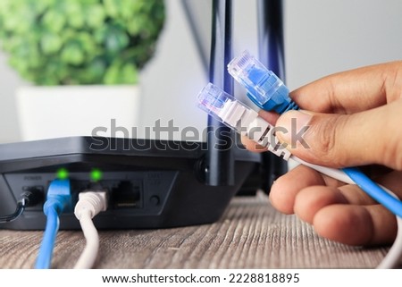 Hand holding Blue and white  Cable Network  RJ45 Lan Internet. router and laptop placed on a wooden table, modem router, Data Center Concept.