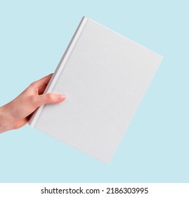 Hand Holding Book Mockup On Blue Background. White Cover Template. Literature, Education, Reading Concept. High Quality Photo