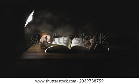 Hand holding a book to read alone in a dark room with a lamp to illuminate.