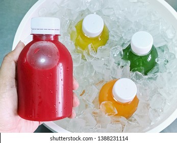 Hand holding the bottle of red color cold pressed fruit and vegetables juice over the ice bucket contain colorful juices.