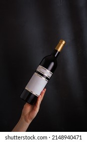 hand holding bottle of red wine with mock up label, no brand on black background. Cabernet sauvignon, merlot, pinot noir. Alcohol drink, copy space