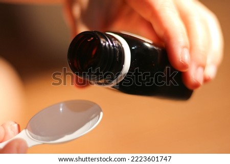 the hand holding the bottle will pour cough syrup onto a plastic spoon. health concept, medicine, syrup medicine, spoon.
